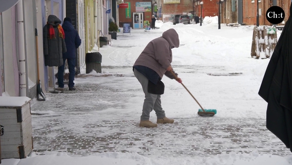 Поки нема покупців продавчиня чистить сніг поблизу свого магазину