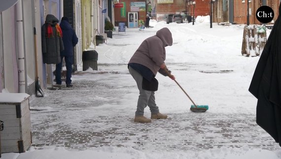 Поки нема покупців продавчиня чистить сніг поблизу свого магазину