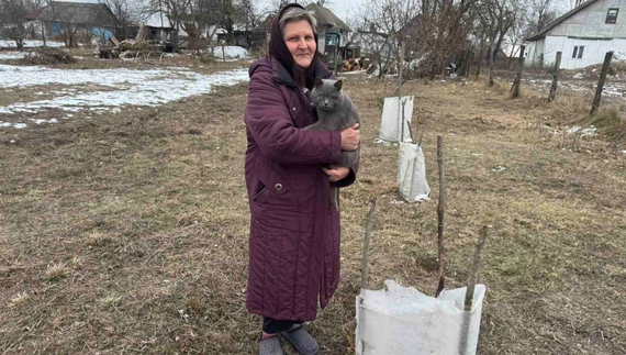 Наталія Одерій з котом Кузею біля дерев, загороджених агроволокном