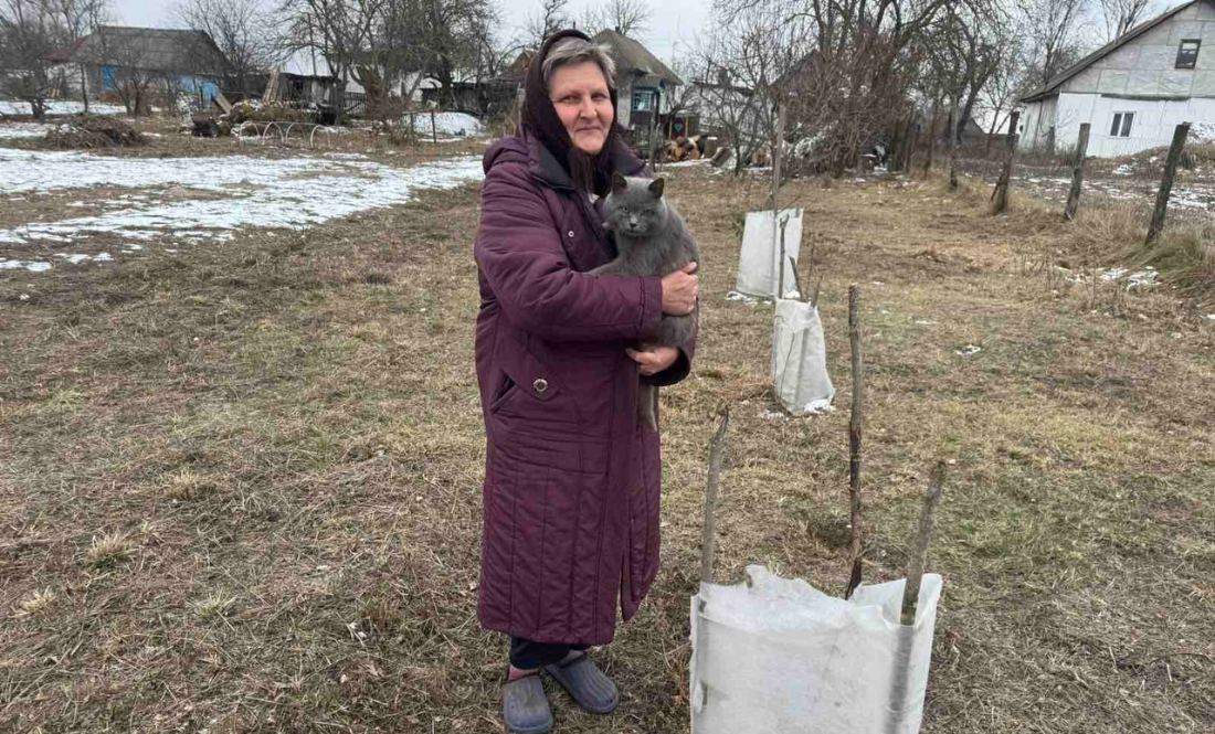 Наталія Одерій з котом Кузею біля дерев, загороджених агроволокном